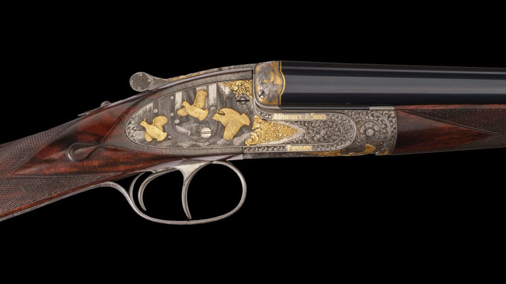Side view of an ornate double-barrel shotgun with gold inlay and intricate engravings on the metal receiver.