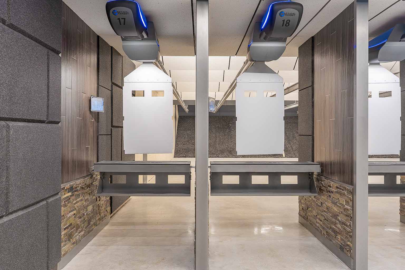 Two empty indoor shooting range lanes with target carriers and protective barriers, viewed from behind the firing line.