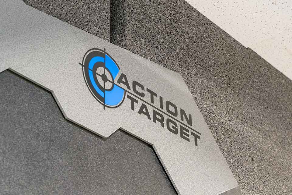 A metallic sign reads "Action Target" with a blue and black target logo on a gray textured wall.